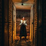 A girl, a woman in traditional Ukrainian clothing stands in a dark basement with a candle in her hands. Tragedy in Ukraine, war of shelling, blackout of electricity, light. Vertical photo