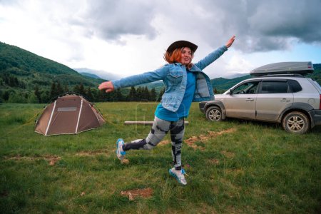 Foto de Mujer saltando por la felicidad, divirtiéndose y bailando en la cima de la montaña. Concepto de viaje y deambulación, tienda y camping. - Imagen libre de derechos