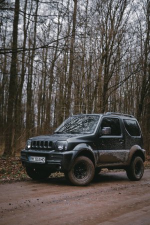Photo for Khmelnytskyi, Ukraine - 01 April 2023: Suzuki Jimny JB43 gray colour. on the dirt road. Forest on background. Four wheel drive vehicle. Cooper discoverer at3 sport2 tyres. Vertical photo. - Royalty Free Image