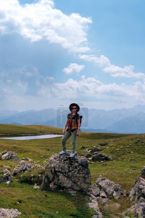 Foto de Una mujer, un turista, un viajero está parado sobre una roca. Punto final de la ruta a pie a los lagos Koruldi, región de Svaneti, Georgia. Día de verano en las montañas del Cáucaso. Foto vertical - Imagen libre de derechos