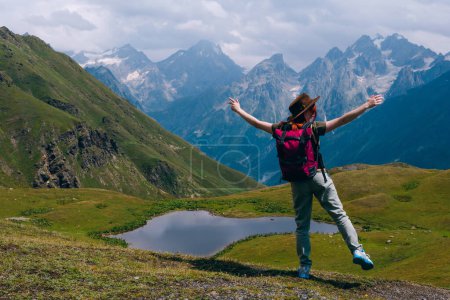 Téléchargez les photos : Une femme Debout les bras écartés sur les côtés. au lac Koruldi avec vue sur la montagne Mestia dans la chaîne de montagnes du Caucase, Haute Svaneti, Pays de Géorgie. La soif d'errance. Trekking. Espace de copie - en image libre de droit