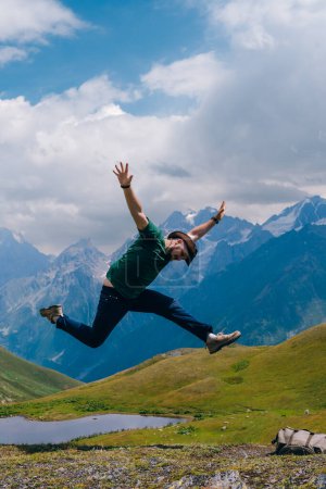 Téléchargez les photos : Un homme plaisir touristique saut avec happines près du lac Koruldi, Mestia dans la chaîne de montagnes du Grand Caucase Haute Svaneti, Géorgie. voyages et vacances. Jour d'été. Photo verticale - en image libre de droit