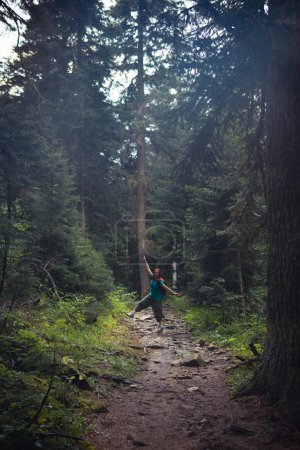 Téléchargez les photos : Une femme avec un sac à dos, une randonneuse, marche le long d'un sentier pierreux au milieu d'une forêt dense. concept de voyage. Sentier jusqu'à la cascade de Shdugra. Montagne Caucase Géorgie, région de Svaneti. Photo verticale - en image libre de droit