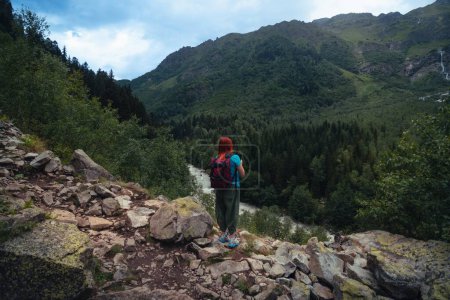 Téléchargez les photos : Une femme regarde la rivière Dolra, une randonneuse, se promène le long d'un sentier pierreux. concept de voyage. Sentier jusqu'à la cascade de Shdugra. Chaîne de montagnes du Caucase en Géorgie, région de Svaneti. La soif d'errance. - en image libre de droit