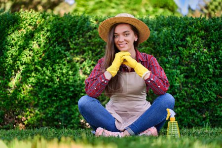 Photo for Portrait of happy smiling woman gardener wearing straw hat, apron and yellow rubber gloves in green garden on lush bush background - Royalty Free Image