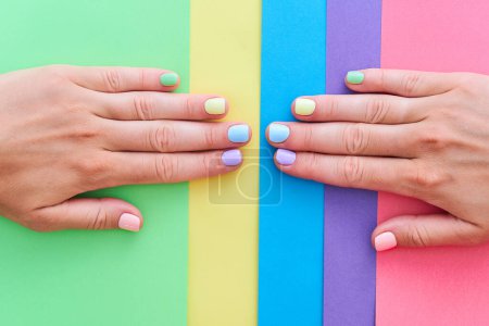 Foto de Manos femeninas con uñas de color brillante sobre un fondo colorido - Imagen libre de derechos