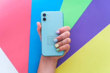 Photo for Female hands with color manicure holds green mint colored phone with dual lenses on a bright colorful background. Top view - Royalty Free Image