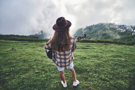 Téléchargez les photos : Jeune voyageuse hipster gratuit avec guitare pendant une escapade dans les montagnes. Musique country - en image libre de droit