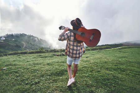 Téléchargez les photos : Jeune voyageuse hipster gratuit avec guitare tout en voyageant à la montagne. Musique country - en image libre de droit