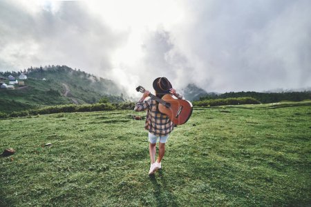 Téléchargez les photos : Jeune voyageuse hipster gratuit avec guitare tout en voyageant à la montagne. Musique country - en image libre de droit