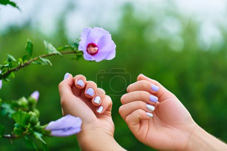 Foto de Manicura femenina con esmalte de uñas de color y brillo plateado sobre el fondo de las flores en un parque al aire libre - Imagen libre de derechos