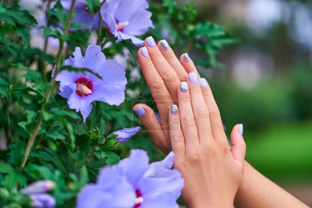 Photo for Female manicure with color nail polish and silver glitter against the background of flowers in a park outdoors - Royalty Free Image