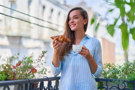 Photo for Portrait of a beautiful happy cute joyful smiling romantic woman with coffee cup and fresh baked croissant for french breakfast in the morning on a balcony - Royalty Free Image