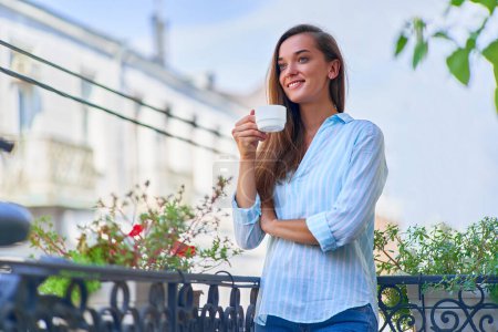 Téléchargez les photos : Portrait d'une belle femme heureuse et joyeuse souriante romantique avec une tasse de café aromatique dans les mains le matin sur un balcon - en image libre de droit