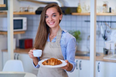 Photo for Portrait of a beautiful happy cute joyful smiling pastry chef woman with a plate of fresh baked sweet brown croissant and coffee cup - Royalty Free Image