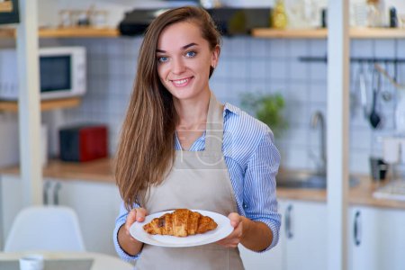 Téléchargez les photos : Portrait d'une belle femme joyeuse et joyeuse chef pâtissier souriant avec une assiette de croissant brun doux frais cuit au four - en image libre de droit