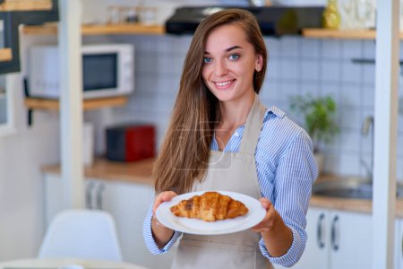Photo for Portrait of a beautiful happy cute joyful smiling pastry chef woman with a plate of fresh baked sweet brown croissant - Royalty Free Image