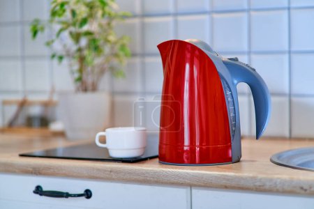 Téléchargez les photos : Bouilloire électrique rouge moderne avec une tasse blanche sur la table dans la cuisine à la maison - en image libre de droit