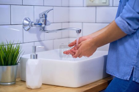 Photo for Person washes hands in the bathroom sink with liquid antibacterial soap. Daily protection and prevention from viruses, microbes and bacteria - Royalty Free Image