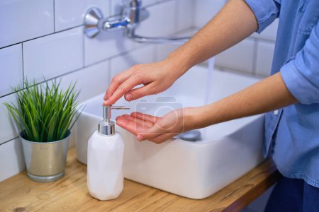 Photo for Person washes hands in the bathroom sink with liquid antibacterial soap. Daily protection and prevention from viruses, microbes and bacteria - Royalty Free Image