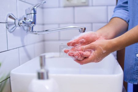 Foto de La persona se lava las manos en el lavabo del baño con jabón líquido antibacteriano. Protección diaria y prevención frente a virus, microbios y bacterias - Imagen libre de derechos