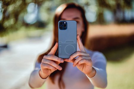 Casual woman takes a photo on a modern smartphone camera outdoors                          