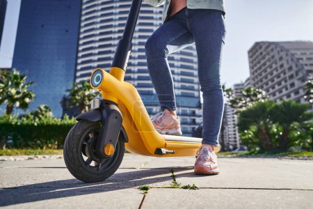 Téléchargez les photos : Femme moderne décontractée utilisant un scooter électrique pour une équitation écologique rapide à travers la ville - en image libre de droit