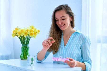 Photo for Young smiling attractive happy woman taking dietary supplement vitamin omega 3 for women's health support. Fish oil softgel, vitamin D and C for immunity and disease prevention - Royalty Free Image