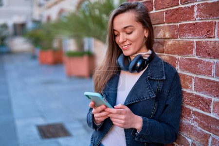 Photo for Portrait of modern smiling happy casual young woman using wireless headphones and smartphone outdoors - Royalty Free Image