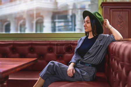 Téléchargez les photos : Élégant élégant élégant un pensif femme hipster réfléchi voyageur portant chapeau en feutre reposant et assis seul près de la fenêtre au café magasin - en image libre de droit