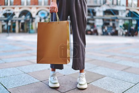 Foto de Elegante mujer adicta a la moda con bolsas de compras de papel camina en el centro de una ciudad europea durante la semana de ventas del viernes negro - Imagen libre de derechos