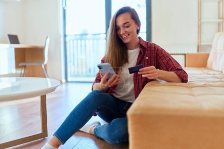 Photo for Beautiful casual happy modern young girl using smartphone and credit card for shopping online, paying and ordering goods via the Internet - Royalty Free Image