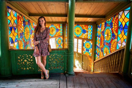 Téléchargez les photos : Jeune fille souriante portant une robe courte debout au balcon kaléidoscopique coloré dans une vieille maison en bois antique à Tbilissi, Géorgie pays - en image libre de droit