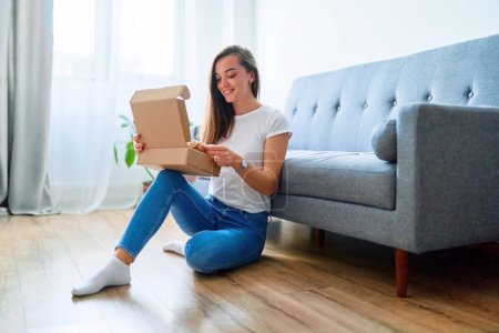 Photo for Happy joyful young satisfied shopaholic woman client sitting on a floor at home and opening received carton parcel box after online ordering, easy and fast service commerce delivery concept - Royalty Free Image