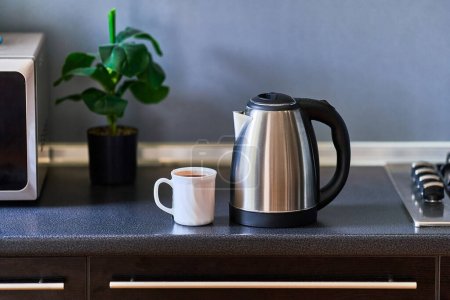 Foto de Moderno hervidor de agua inoxidable de metal plateado y blanco una taza de vidrio para preparar té en la cocina en casa - Imagen libre de derechos