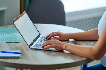 Téléchargez les photos : Mains féminines tapant sur le clavier de l'ordinateur portable avec affichage blanc blanc ouvert sur la table à l'espace de travail. Modèle d'ordinateur pour la publicité en ligne de site Web - en image libre de droit