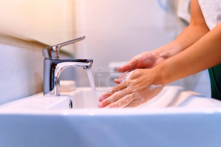 Photo for Female washing her hands using liquid disinfectant soap and running water in bathroom close up. Personal hand hygiene, health care - Royalty Free Image