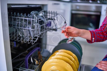 Téléchargez les photos : Femme au foyer utilisant un lave-vaisselle moderne pour laver la vaisselle et les lunettes à la maison cuisine - en image libre de droit