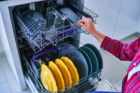 Téléchargez les photos : Femme au foyer utilisant un lave-vaisselle moderne pour laver la vaisselle à la maison cuisine - en image libre de droit