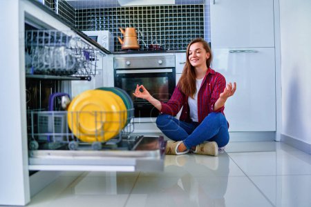 Photo for Young joyful happy housewife woman using modern dishwasher for wash dishes and glasses at white home kitchen. Relax and enjoy during cleaning chores - Royalty Free Image