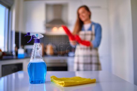 Foto de Ama de casa limpiando el hogar usando una botella de spray desinfectante, guantes de goma protectores rojos y trapo amarillo - Imagen libre de derechos