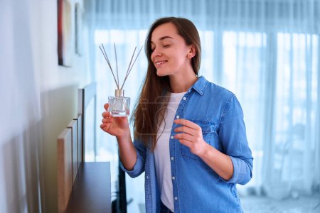 Téléchargez les photos : Jeune femme appréciant l'arôme et l'odeur de désodorisant roseau dans le salon à la maison - en image libre de droit