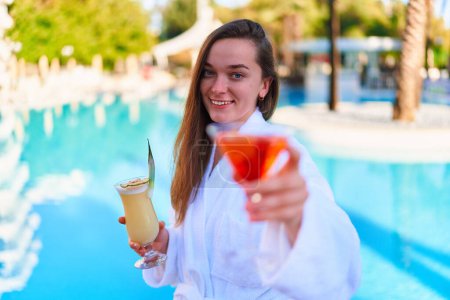 Téléchargez les photos : Young happy smiling joyful woman enjoy of summer vacations with refreshing pina colada and aperol cocktails by the pool at the all-inclusive resort - en image libre de droit