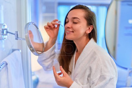 Téléchargez les photos : Young beautiful smiling happy female applies a nourishing serum to moisturize skin after shower. Face skin care - en image libre de droit