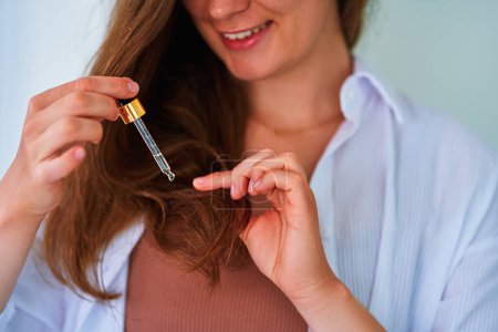 Foto de Mujer morena usando gotero para mimar e hidratar las puntas del cabello con suero de aceite esencial de vitamina - Imagen libre de derechos