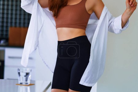 Photo for Sexual fitness woman with beautiful  thin fit body figure and slim waist wearing sportive cycling shorts, brown top and white shirt - Royalty Free Image