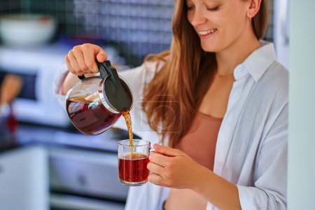 Foto de Feliz hermosa alegre sin preocupaciones satisfecha atractiva mujer beber té negro caliente en casa cocina - Imagen libre de derechos