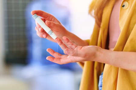 Téléchargez les photos : Femme utilisant lanceter sur le doigt pour mesurer et vérifier le taux de glucose dans le sang. Soins de santé et traitement du diabète sucré - en image libre de droit