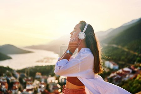 Photo for Inspired happy serene female with closed eyes enjoying of listening calm music with beautiful view at sunset time. Relief stress and healthy minds - Royalty Free Image