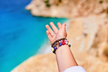 Téléchargez les photos : Main de voyageur fille avec des bracelets menant à la mer à la journée ensoleillée - en image libre de droit